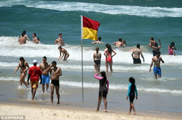Image shows people standing in the water at the beach with the red and yellow flag