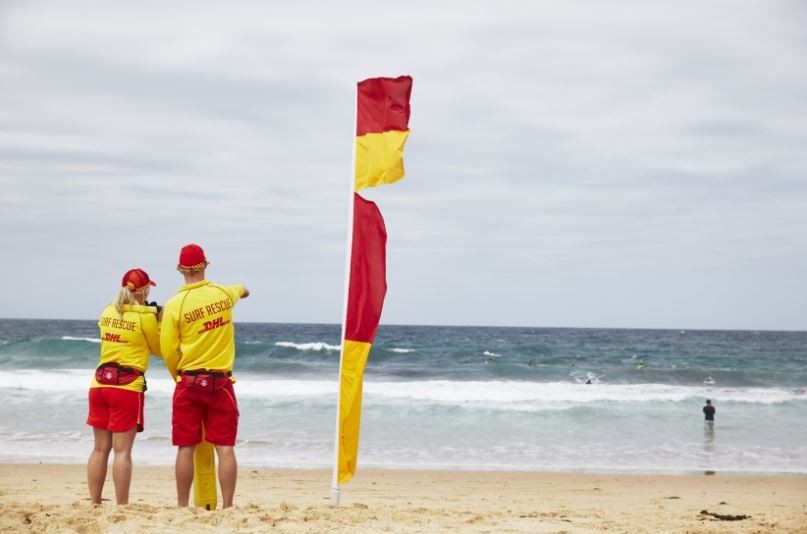 Two lifesavers standing next to a red and yellow flag at the beach. What is a rip current?