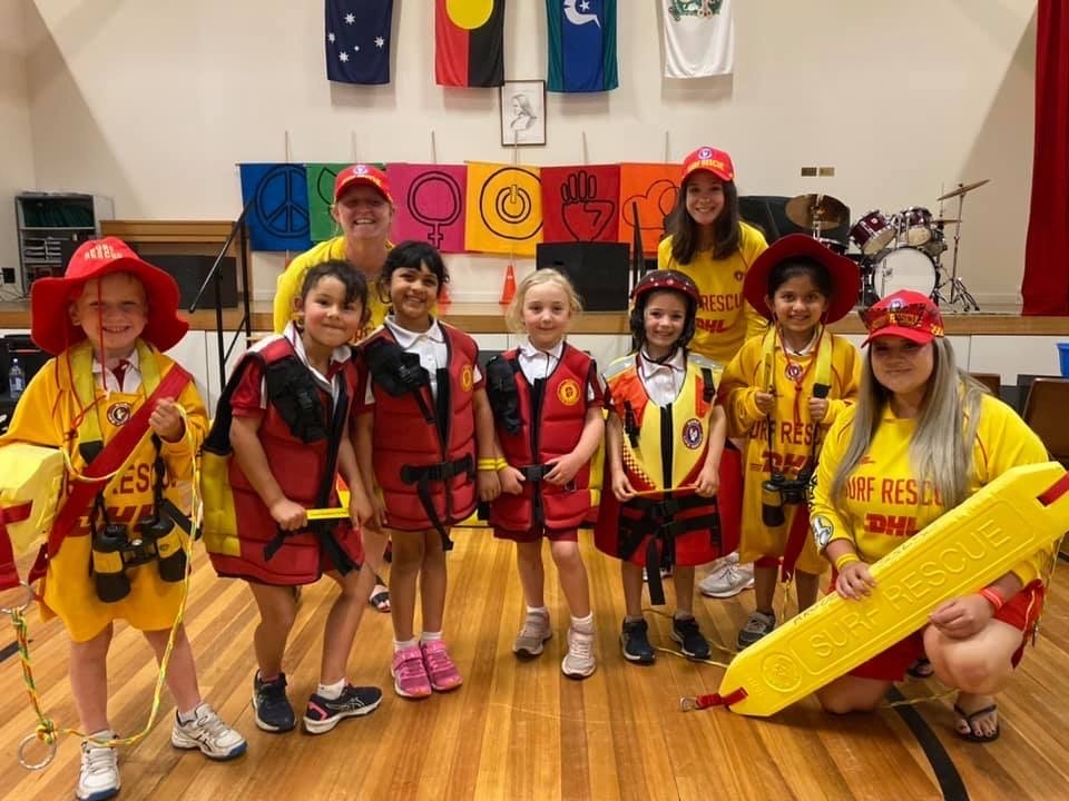 Primary aged school children dressed in lifesaving uniforms with a volunteer surf life saver